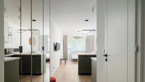 Een moderne hotelkamer met een kitchenette, een eettafel en een groot raam met gordijnen.