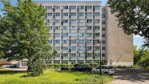 Een meerlaags woongebouw met balkons, een parkeerplaats en omliggend groen.