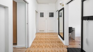 A hallway with a wooden floor, white walls, and a black-framed mirror. There are doors at the end of the hallway and a bench to the right. - Metro Młynów Comfort Apartment (Warszawa)