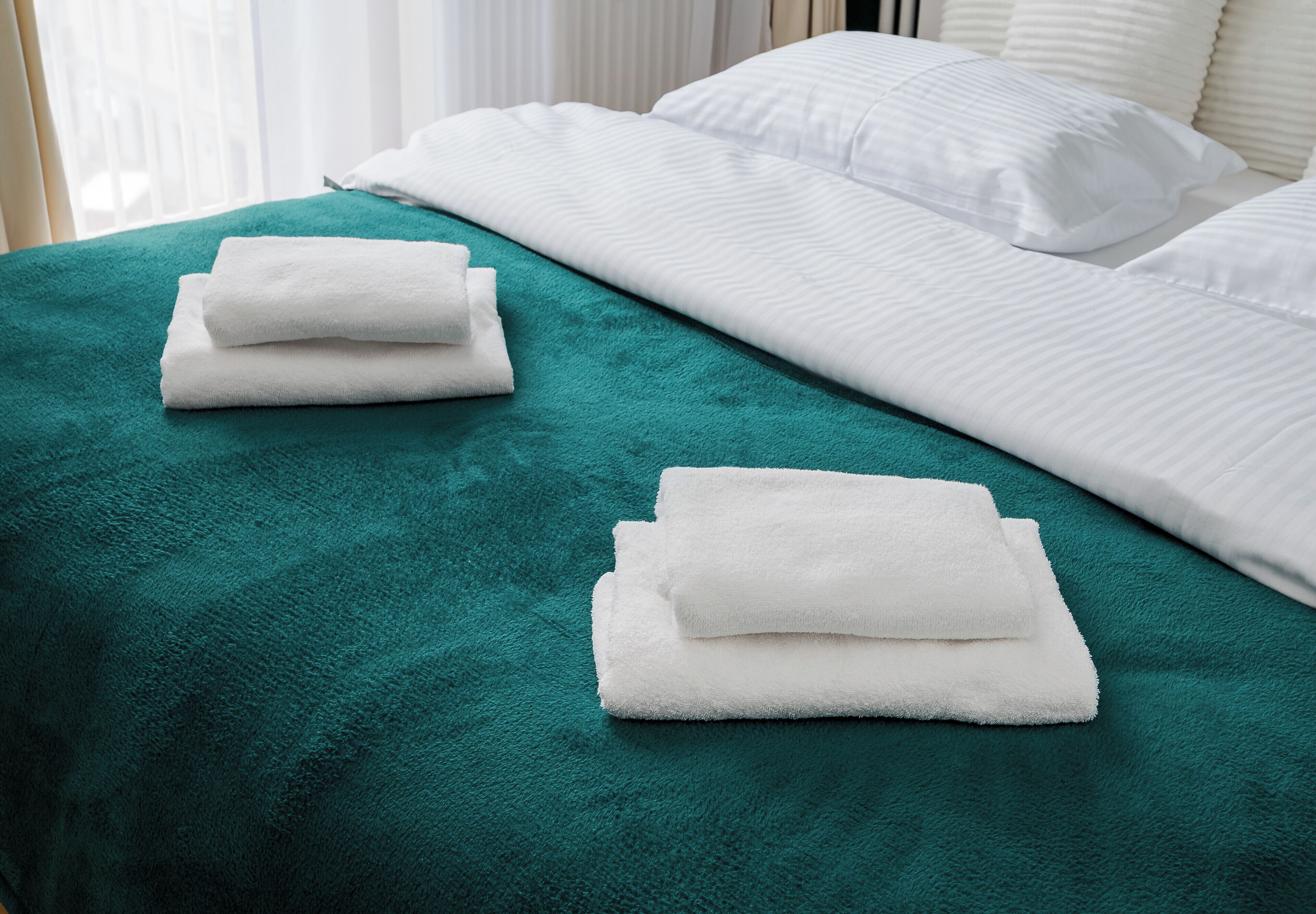 A neatly made bed with white linens and a teal bedspread.