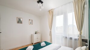 A hotel room with a neatly made bed, a small bedside table with a plant, and a window with sheer curtains. - Złota Warsaw Skyline Apartment (Warszawa)