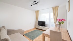 A modern living room with a sofa, a dining table, a TV, and a vase with flowers. - Złota Warsaw Skyline Apartment (Warszawa)