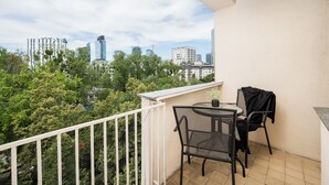 A balcony with a table and chairs, a potted plant, and a view of a cityscape with buildings and trees. - Złota Warsaw Skyline Apartment (Warszawa)