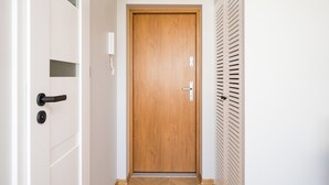 Ein Flur mit einer Holztür, einer weißen Wand und einem Lüftungsgitter auf der rechten Seite.