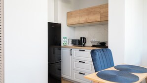 Eine kompakte Küche mit einem schwarzen Kühlschrank, weißen Schränken, einer Holz Arbeitsplatte und einem blauen Stuhl mit rundem Tisch.
