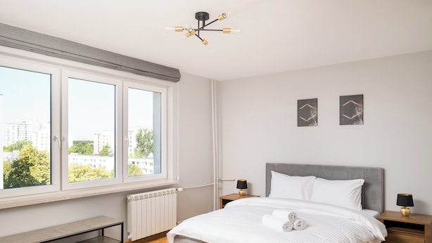 Ein modernes Schlafzimmer mit großem Fenster, einem Bett mit weißer Bettwäsche, zwei Nachttischen mit Lampen und einer Bank am Fenster.