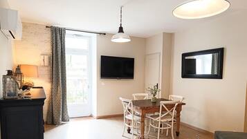 A dining area with a wooden table and white chairs, a television mounted on the wall, and a window with curtains.