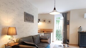 Un salon chaleureux avec un canapé, une lampe et un mur recouvert de notes manuscrites. Au fond, on aperçoit un coin cuisine avec une fenêtre donnant sur un paysage verdoyant.