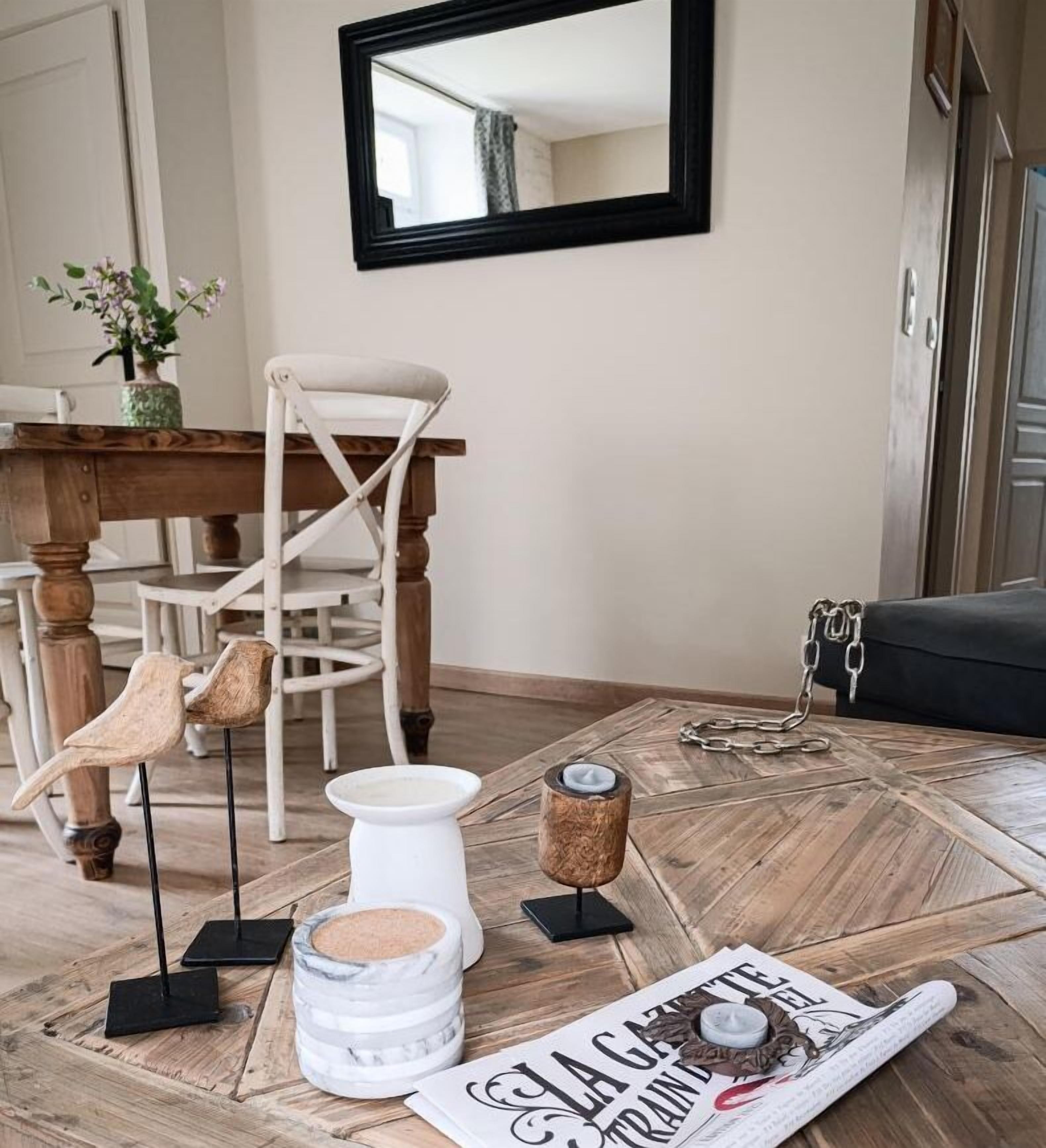 A dining area with a wooden table, chairs, a mirror, and a magazine on the floor.