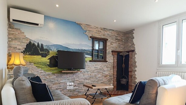 Een woonkamer met een stenen muur, een wandtelevisie, een open haard en een groot raam.