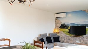Een eetruimte met een houten tafel, stoelen en een kroonluchter. Er is een stenen muur met een televisie en een landschapsmuurdecoratie.