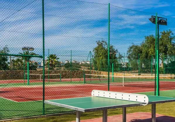 A tennis court with a green net and a table tennis table in the foreground.