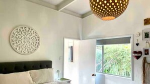 Une chambre à coucher avec un lit, un élément décoratif mural, une fenêtre donnant sur un beau paysage et un luminaire suspendu.