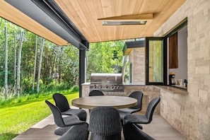 An outdoor patio with a round table and chairs, a grill, and a stone wall. - RMR: Tensleep Oasis Home in The Aspens/Wilson,WY (Wilson)
