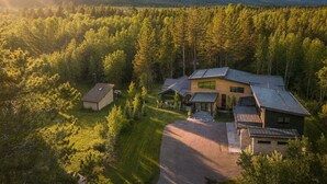 A modern house with a sloped roof, surrounded by a forest and mountains in the background. - RMR: Tensleep Oasis Home in The Aspens/Wilson,WY (Wilson)