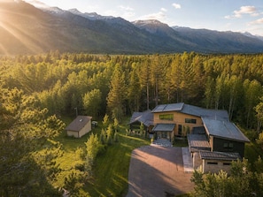 A modern house with a sloped roof, surrounded by a forest and mountains in the background.