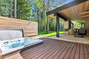 A hot tub on a wooden deck with a covered patio area and a stone fireplace.