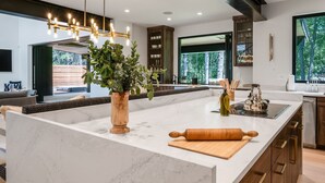 A modern kitchen with a large island, wooden cabinets, and a view of the outdoors. - RMR: Tensleep Oasis Home in The Aspens/Wilson,WY (Wilson)