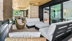 A modern outdoor living area with a stone wall, wooden ceiling, and large sliding glass doors leading to an indoor space. - RMR: Tensleep Oasis Home in The Aspens/Wilson,WY (Wilson)