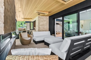 A modern outdoor living area with a stone wall, wooden ceiling, and large sliding glass doors leading to an indoor space.
