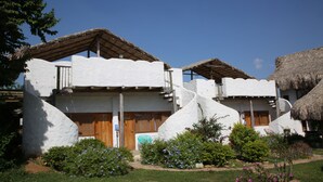 Un edificio tradicional de color blanco con techo de paja, puertas de madera y un pequeño jardín con diversas plantas y flores.