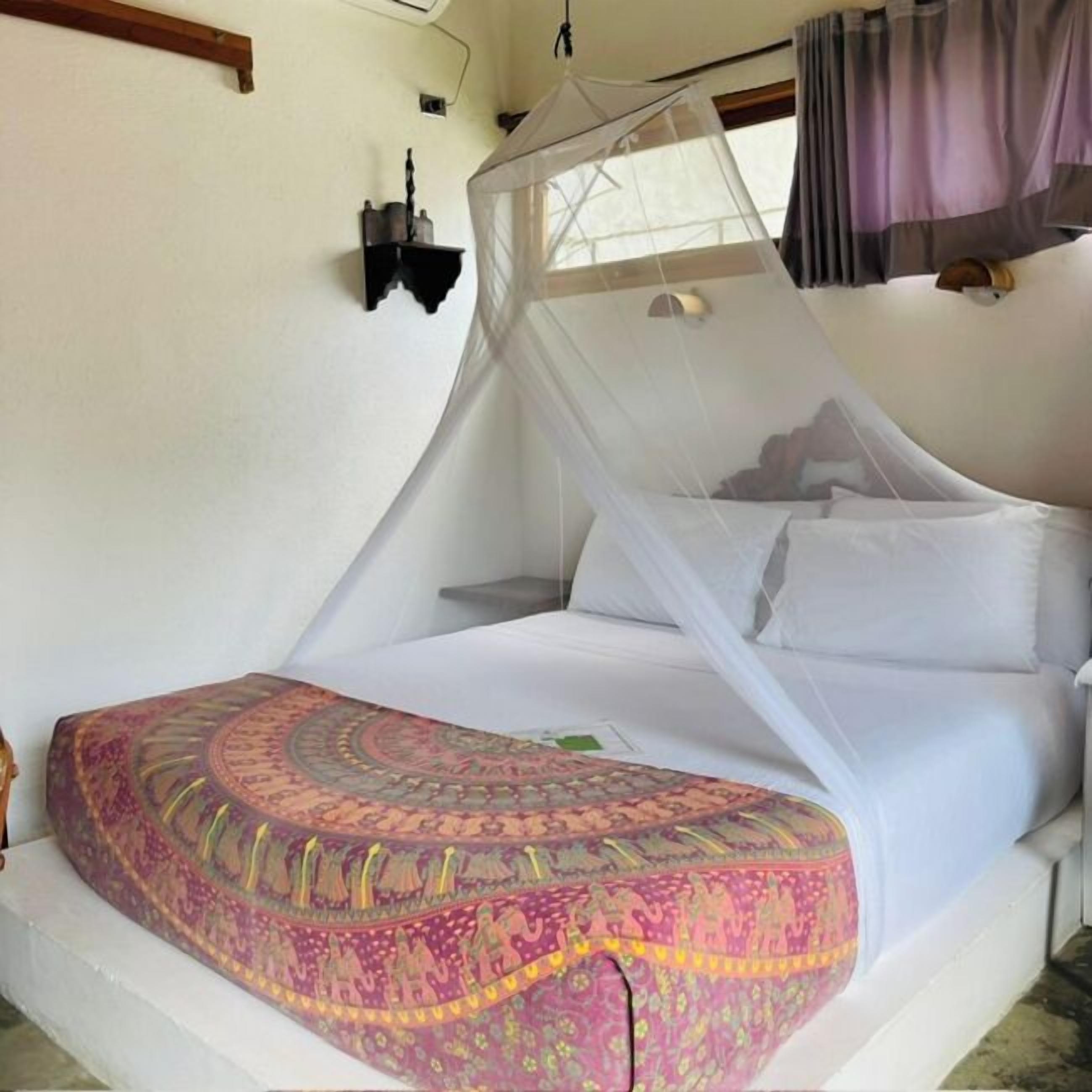 Una cama con dosel, una alfombra estampada y una lámpara fijada en la pared.