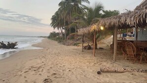 Una playa con una cabaña de techo de paja y una estructura de madera con sillas.