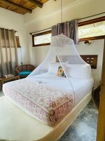 Una cama individual con dosel, una mesita de noche y una silla en una habitación con techo de madera y ventana con cortinas.