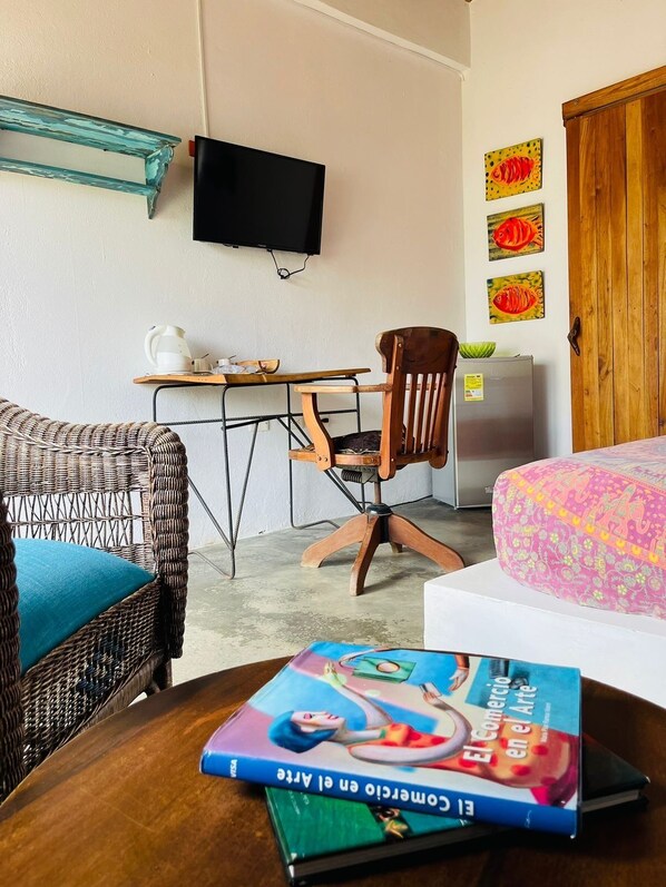 A room with a wicker chair, a wooden desk, a television, a bed with a patterned bedspread, and a book on the table. - Casa Dibulla Hotel Boutique (Dibulla)