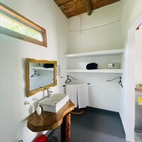 Un baño con tocador de madera, un espejo con marco decorativo, un lavabo blanco, un perchero y un estante con una radio.