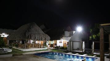 Un área de piscina con una estructura de techo de paja, una piscina pequeña y un área de descanso con mesas y sillas.