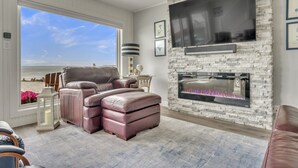 A living room with a stone fireplace, leather recliner, and a large window overlooking a beach. - NEW LISTING...AWave From It All - Lakefront on Big Spirit Lake (Orleans)