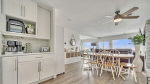 A modern kitchen with white cabinetry, a dining area with wooden chairs, and a ceiling fan. - NEW LISTING...AWave From It All - Lakefront on Big Spirit Lake (Orleans)