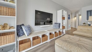 A modern living room with a large flat-screen TV, a beige sofa, and built-in wicker baskets on shelves. - NEW LISTING...AWave From It All - Lakefront on Big Spirit Lake (Orleans)