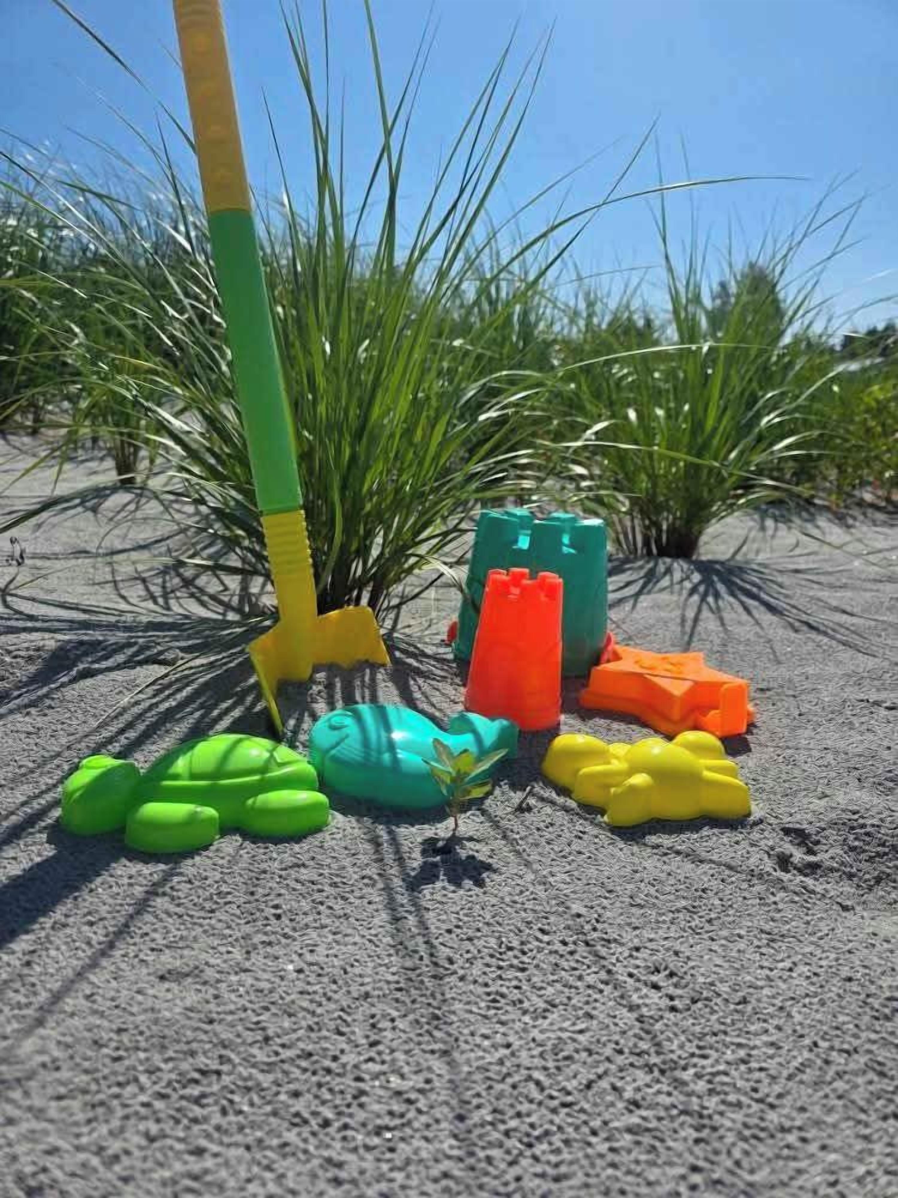 Zona arenosa con una pala, juguetes de plástico de colores y plantas verdes.