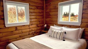 A wooden cabin bedroom with a bed, pillows, and two windows. - Cottage # 1 Hunts Point Beach Cottages - 2 bedrooms (Hunts Point)