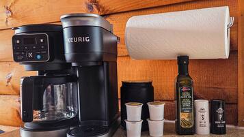 En Keurig-kaffemaskine på en bordplade sammen med en papirhåndklædedispenser, en flaske olivenolie og flere små beholdere.