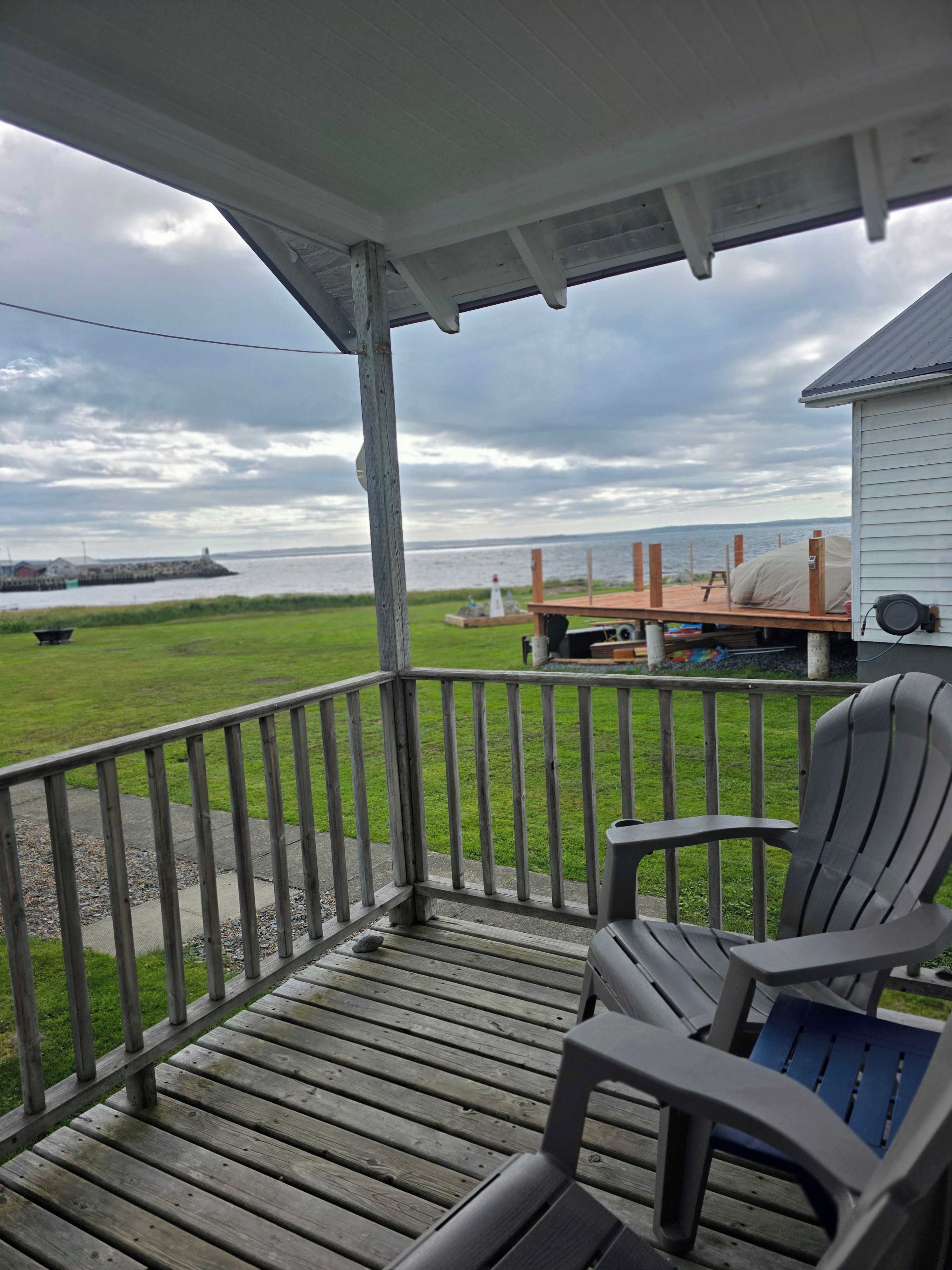 Une terrasse en bois avec deux chaises, un espace abrité et une vue sur l’eau et un phare.