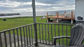 Une terrasse en bois avec deux chaises, un espace abrité et une vue sur l’eau et un phare.