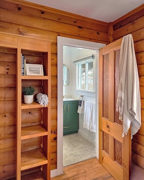 Un intérieur en bois avec une bibliothèque, un meuble vert, une fenêtre et une serviette accrochée au mur.