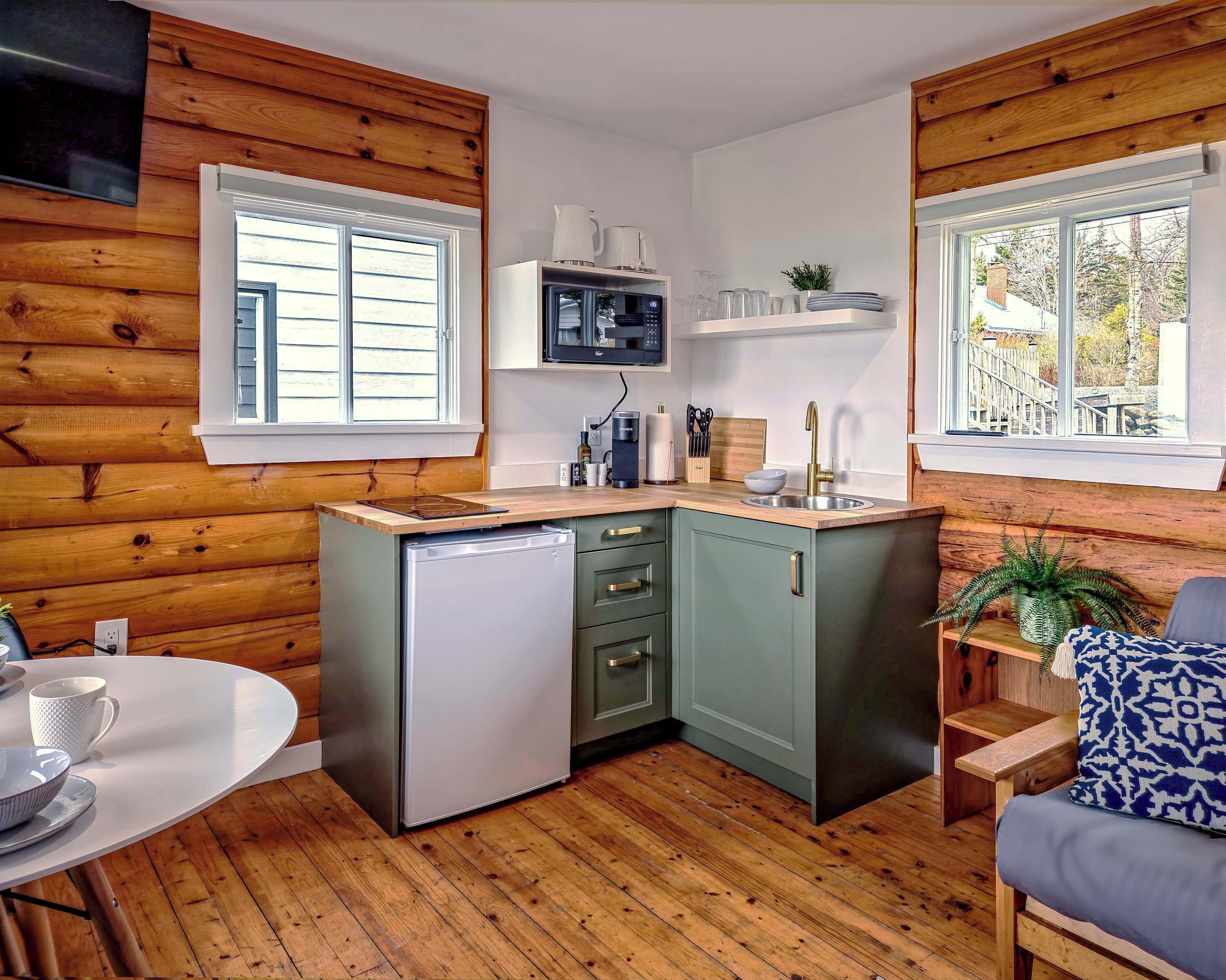 Una cocina compacta con paredes de madera, un microondas integrado, un lavamanos y un refrigerador pequeño.