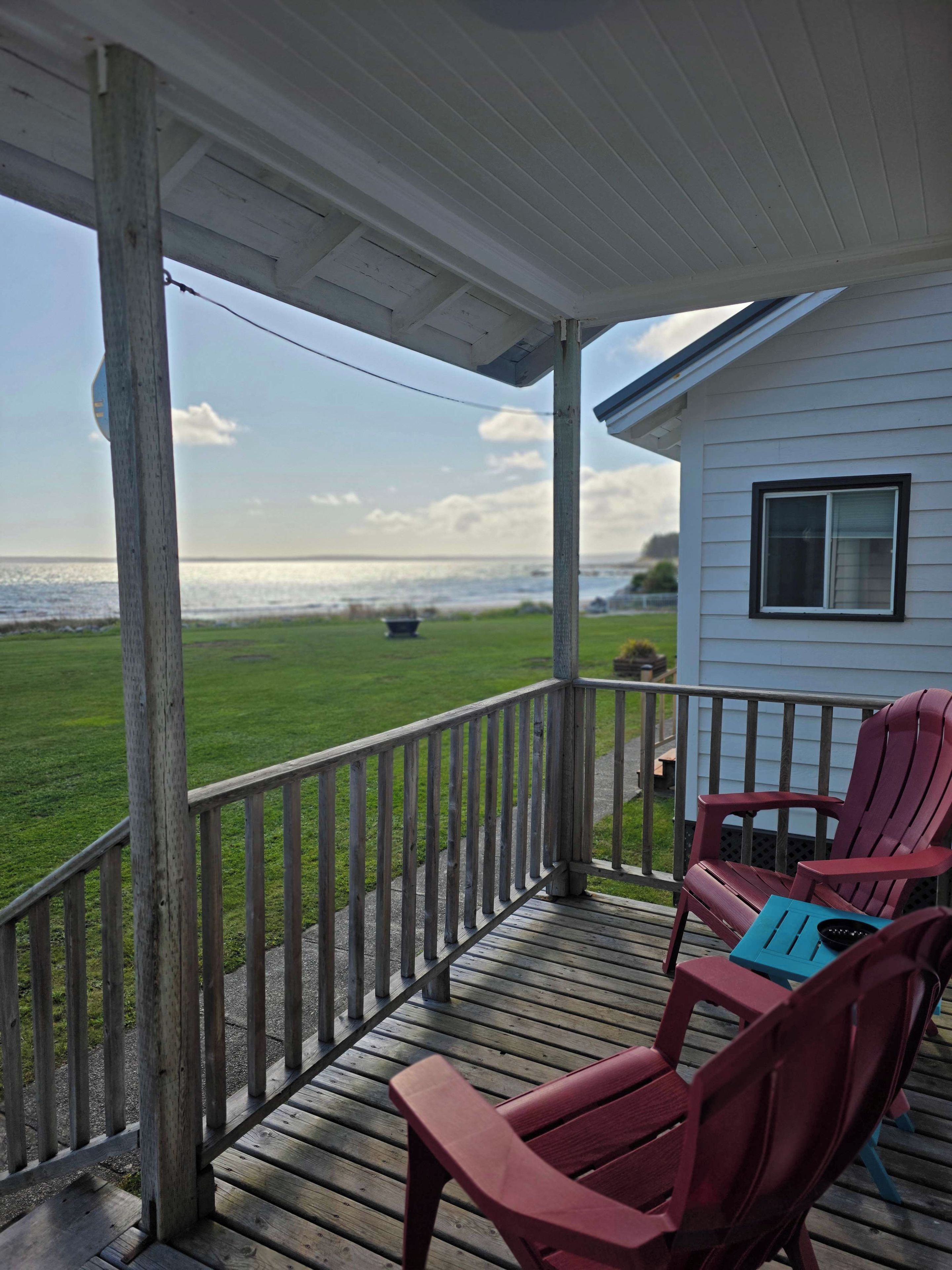A wooden deck with a railing, two Adirondack chairs, and a view of the ocean.