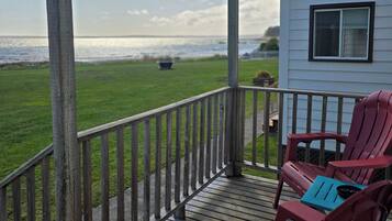 A wooden deck with a railing, two Adirondack chairs, and a view of the ocean.