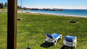 A view from a wooden deck overlooking a grassy area with two blue lounge chairs. - Cottage # 7 Hunts Point Beach Cottages 1 Bedroom (Hunts Point)