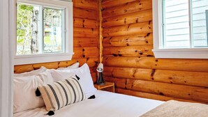 A wooden-paneled room with a bed, two windows, and a nightstand with a lamp. - Cottage # 7 Hunts Point Beach Cottages 1 Bedroom (Hunts Point)