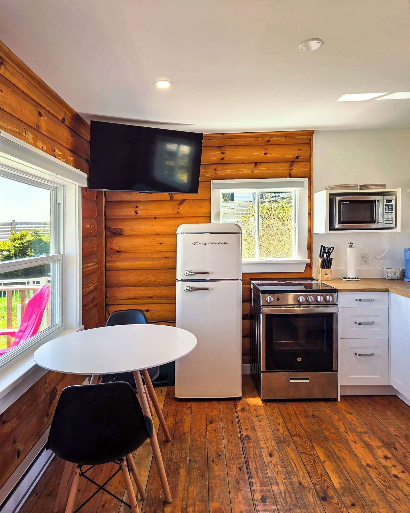 Cocina compacta con refrigerador, estufa, microondas y televisor montado en la pared.