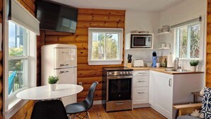 A compact kitchen with a refrigerator, stove, microwave, and sink. There are two chairs and a small table. - Cottage # 9 Hunts Point Beach Cottages - 1 bedroom (Hunts Point)