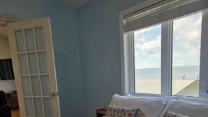 A bedroom with a bed, a window with a view of the sea, and a door leading to another room. - Pent House at Hunts Point Beach Cottages (Hunts Point)