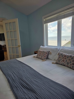 A bedroom with a bed, a window with a view of the sea, and a door leading to another room. - Pent House at Hunts Point Beach Cottages (Hunts Point)