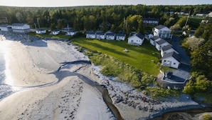 An aerial view of a coastal residential area with houses, a sandy beach, and a narrow water channel. - Pent House at Hunts Point Beach Cottages (Hunts Point)